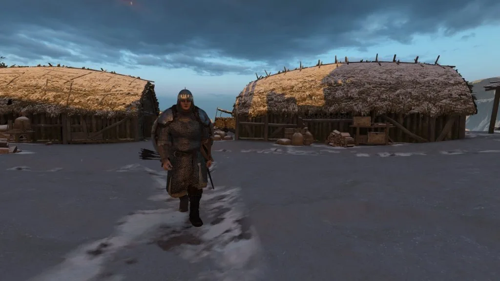 Mount & Blade 2 Bannerlord screenshot of a woman in armor walking along a snowy path, in-between two wooden houses.